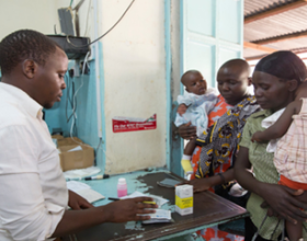 Pharmacist dispenses a prescription to two mothers with young children.